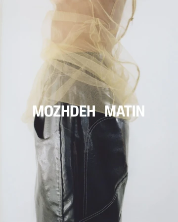 Model wearing sheer yellow top and black trousers against white background with brand text Mozhdeh Matin