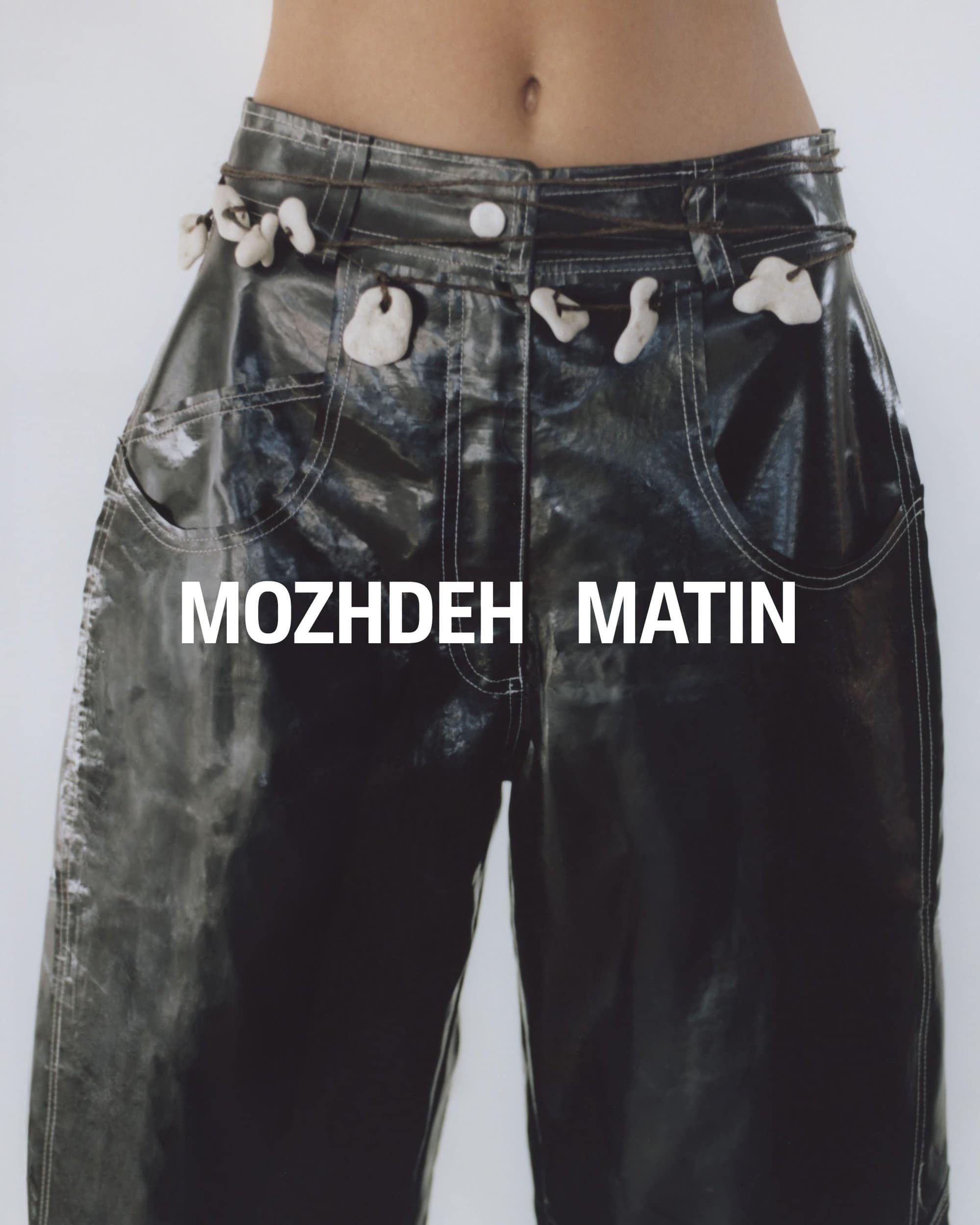 Close-up of shiny dark trousers with white pebble belt accents and bold white text across the waist.