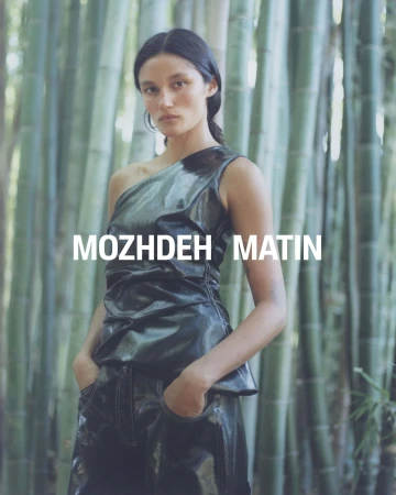 Model standing among bamboo stalks wearing a dark one-shoulder top and matching trousers for Mozhdeh Matin