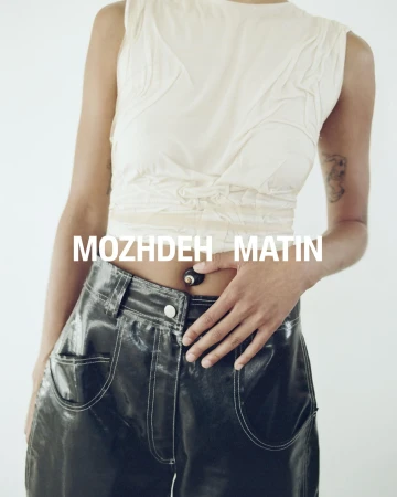 Model wearing a white sleeveless top and dark glossy trousers against a white backdrop for Mozhdeh Matin.