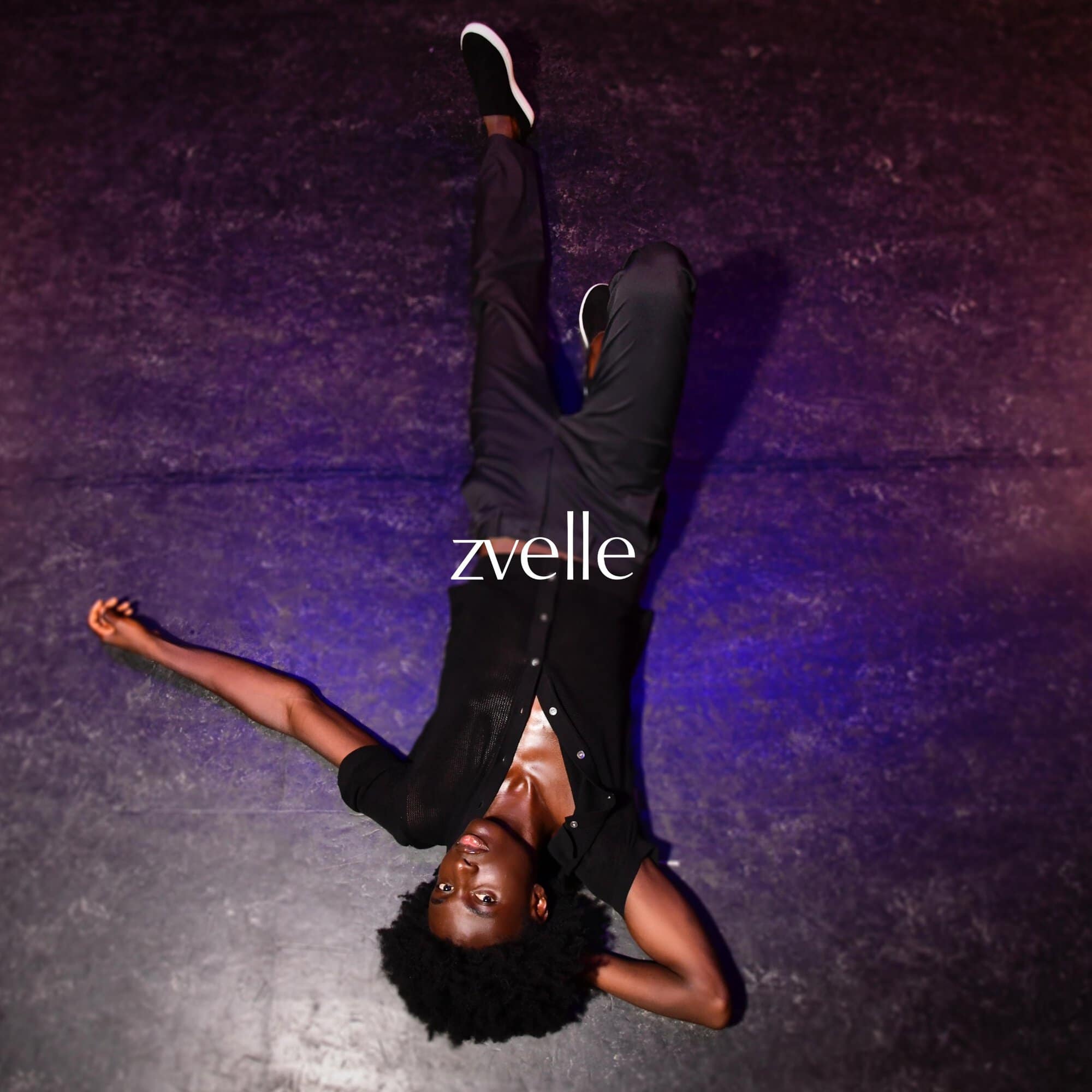 Man lying upside down on a dark textured surface wearing a black button shirt and dark trousers for Zvelle ad campaign