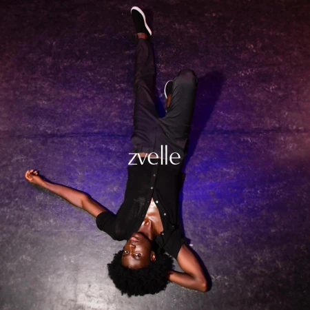 Man lying upside down on a dark textured surface wearing a black button shirt and dark trousers for Zvelle ad campaign