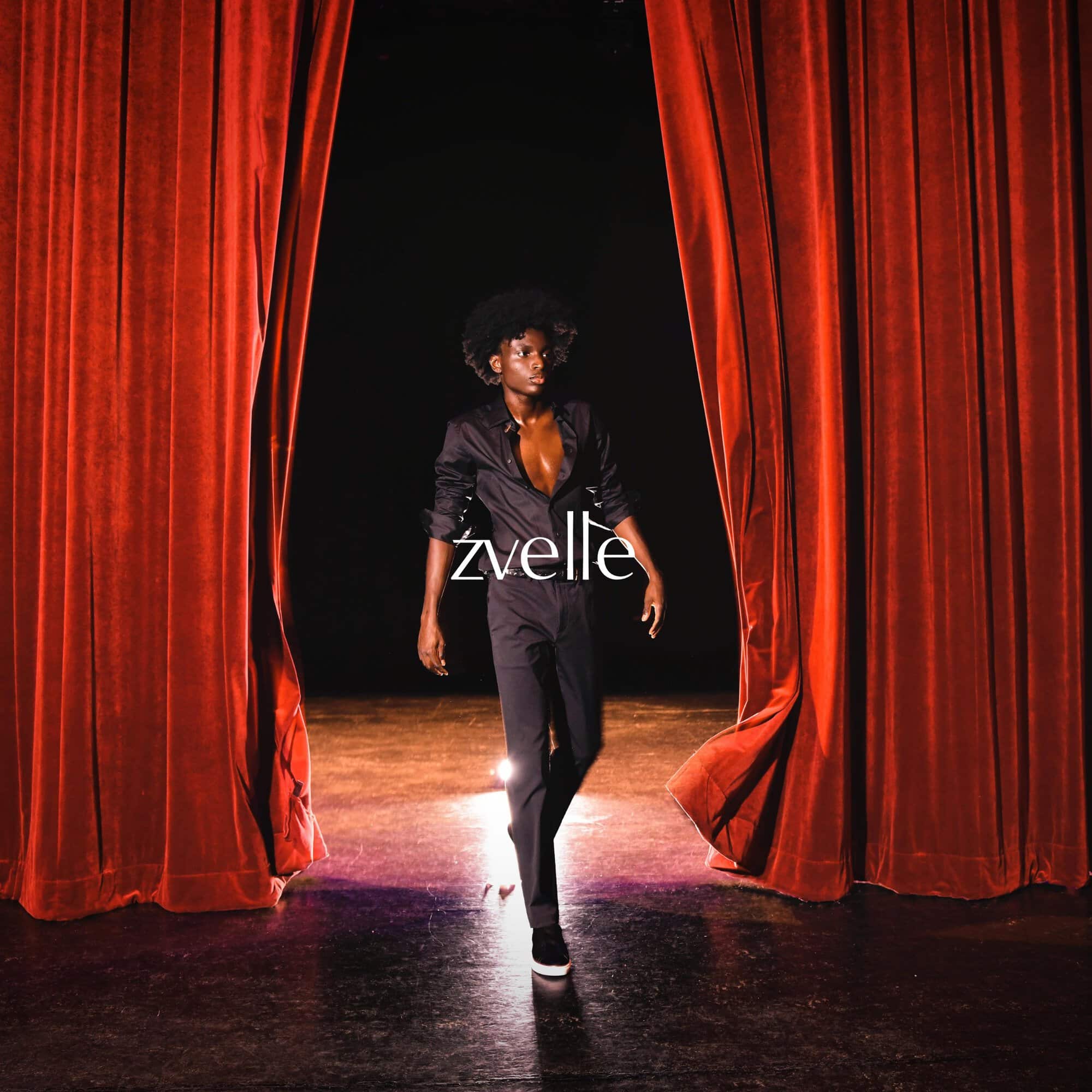 Model walking between heavy red velvet theatre curtains on a wooden stage with dramatic lighting for Zvelle Fall 2024 campaign