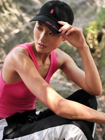 Model wearing a black baseball cap and pink tank top posing outdoors among rocks for Ralph Lauren