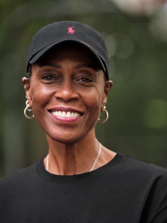 Portrait of a Black woman smiling while wearing a black baseball cap with a pink logo and a black t-shirt