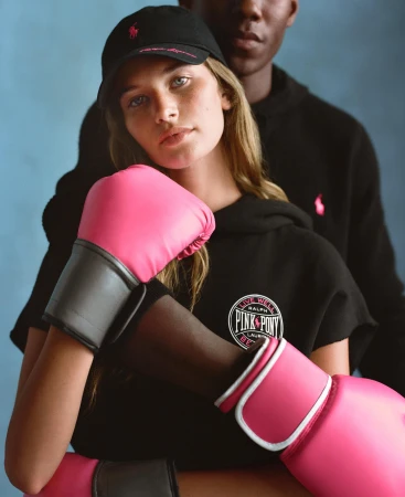 Two models wearing black hoodies and pink boxing gloves posing against a textured blue studio background for Ralph Lauren.