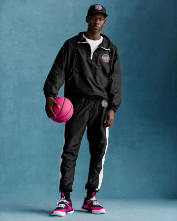 Man wearing a black windbreaker holding a bright pink basketball against a textured blue backdrop