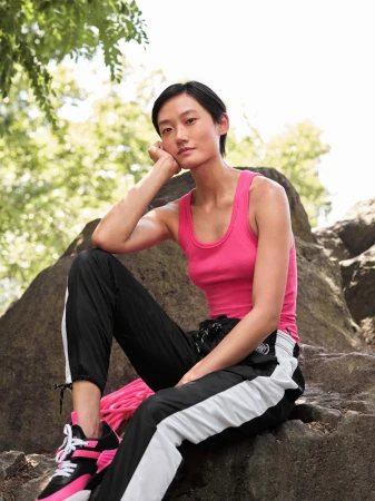 Model wearing hot pink tank top and black track pants seated on rock in park