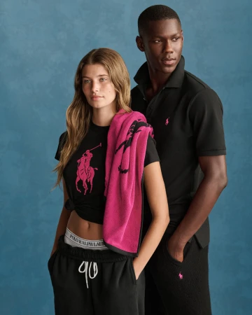 Two models wearing black polo shirts and matching apparel with pink Ralph Lauren branding against a textured blue background