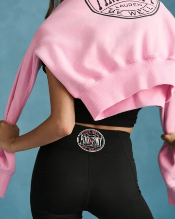 Close-up back view of a person wearing black leggings and a pink sweatshirt draped over shoulders.