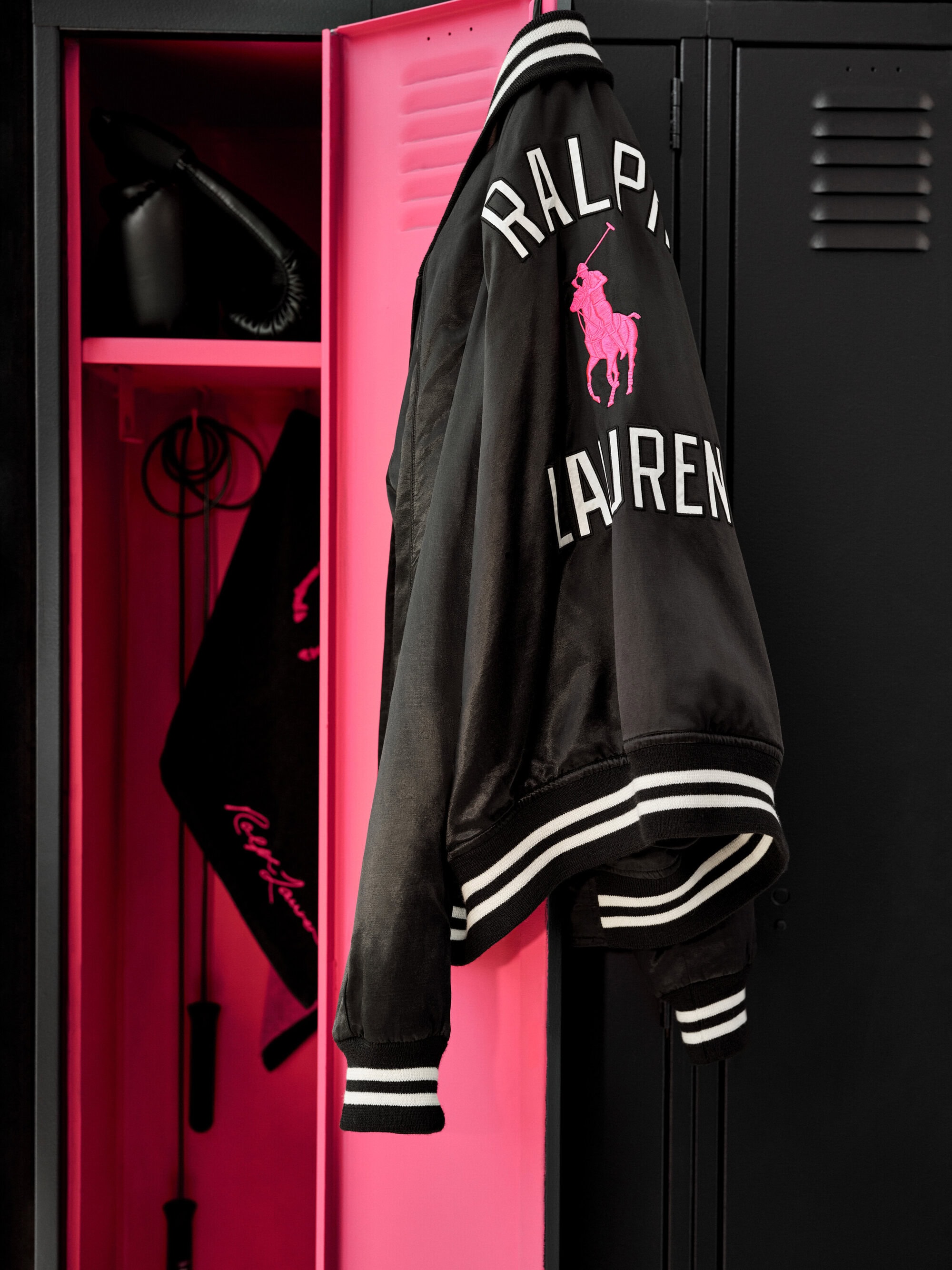 Black and pink varsity jacket hanging on a bright pink locker door with black lockers alongside it.