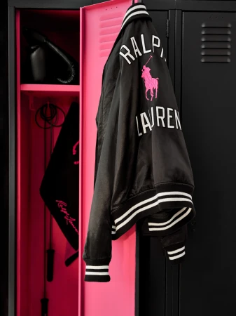 Black and pink varsity jacket hanging on a bright pink locker door with black lockers alongside it.