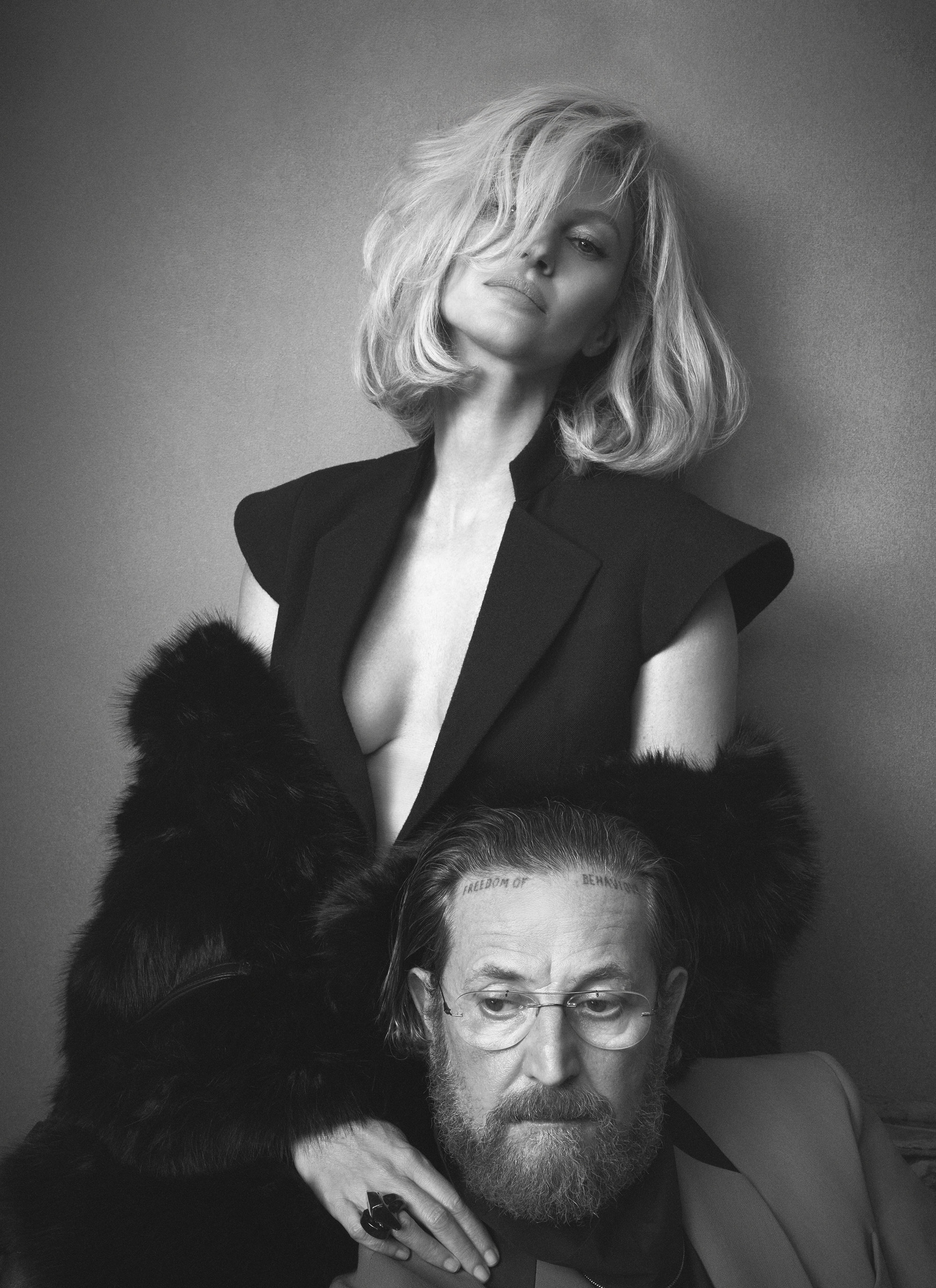 Gisele Bundchen standing behind Stefano Pilati wearing a dark tailored sleeveless top and fur stole in a black and white fashion portrait.