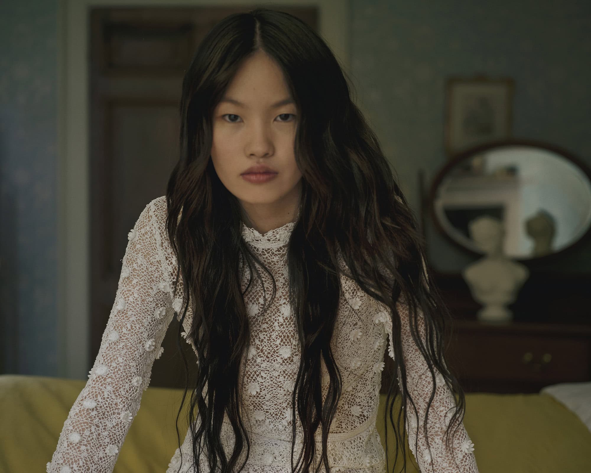 Woman with long dark hair wearing a white lace dress in a domestic room