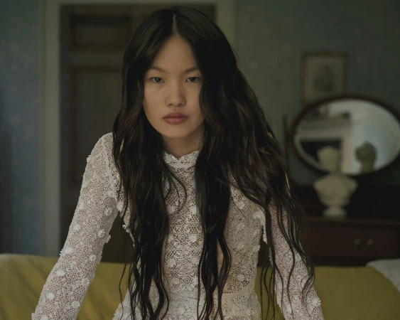 Woman with long dark hair wearing a white lace dress in a domestic room