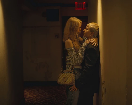 Two people embracing in a dimly lit hallway with a red exit sign, part of Gucci We Will Always Have London campaign.
