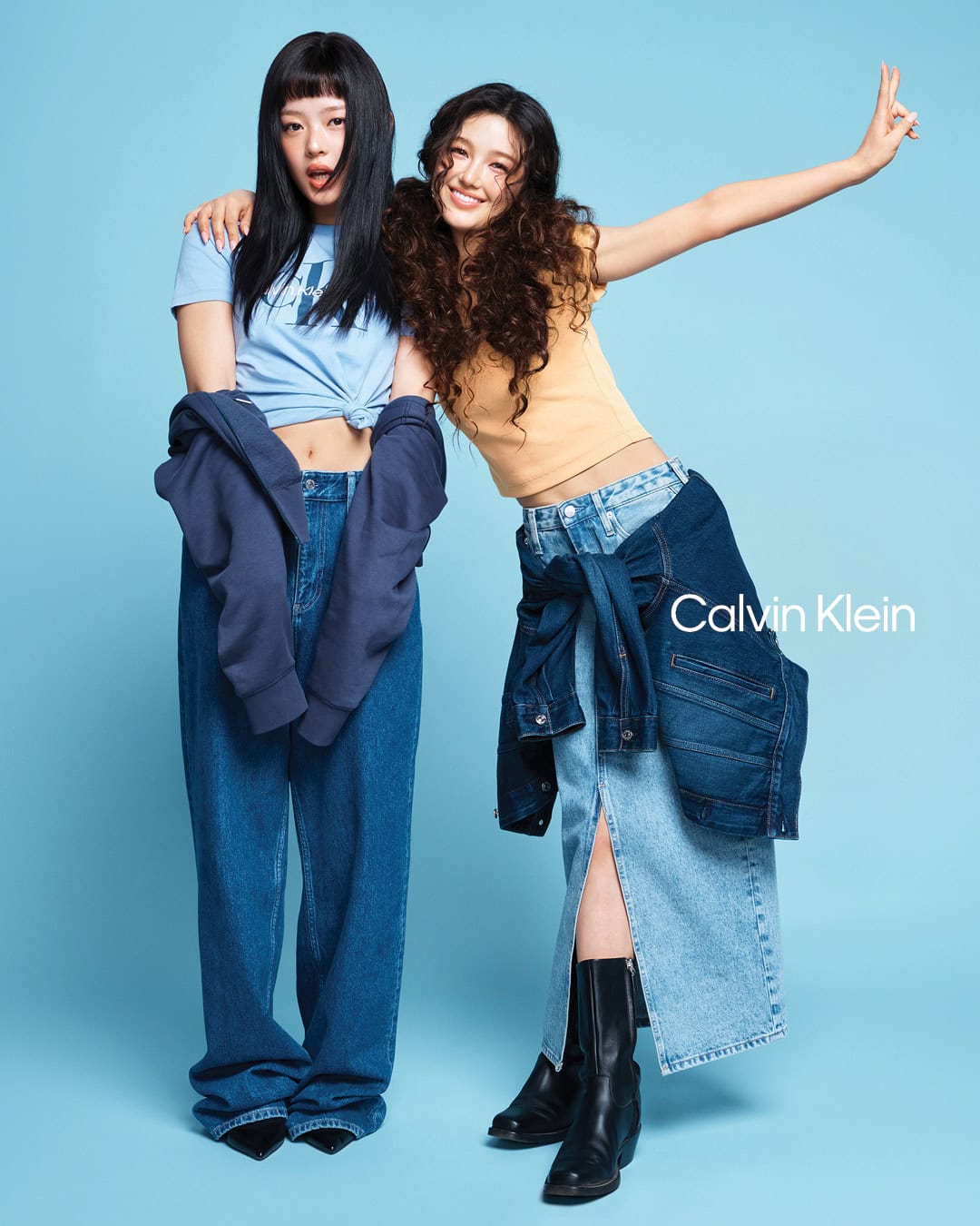 Two young models posing together against a blue background for a Calvin Klein ad campaign wearing casual t-shirts and denim.