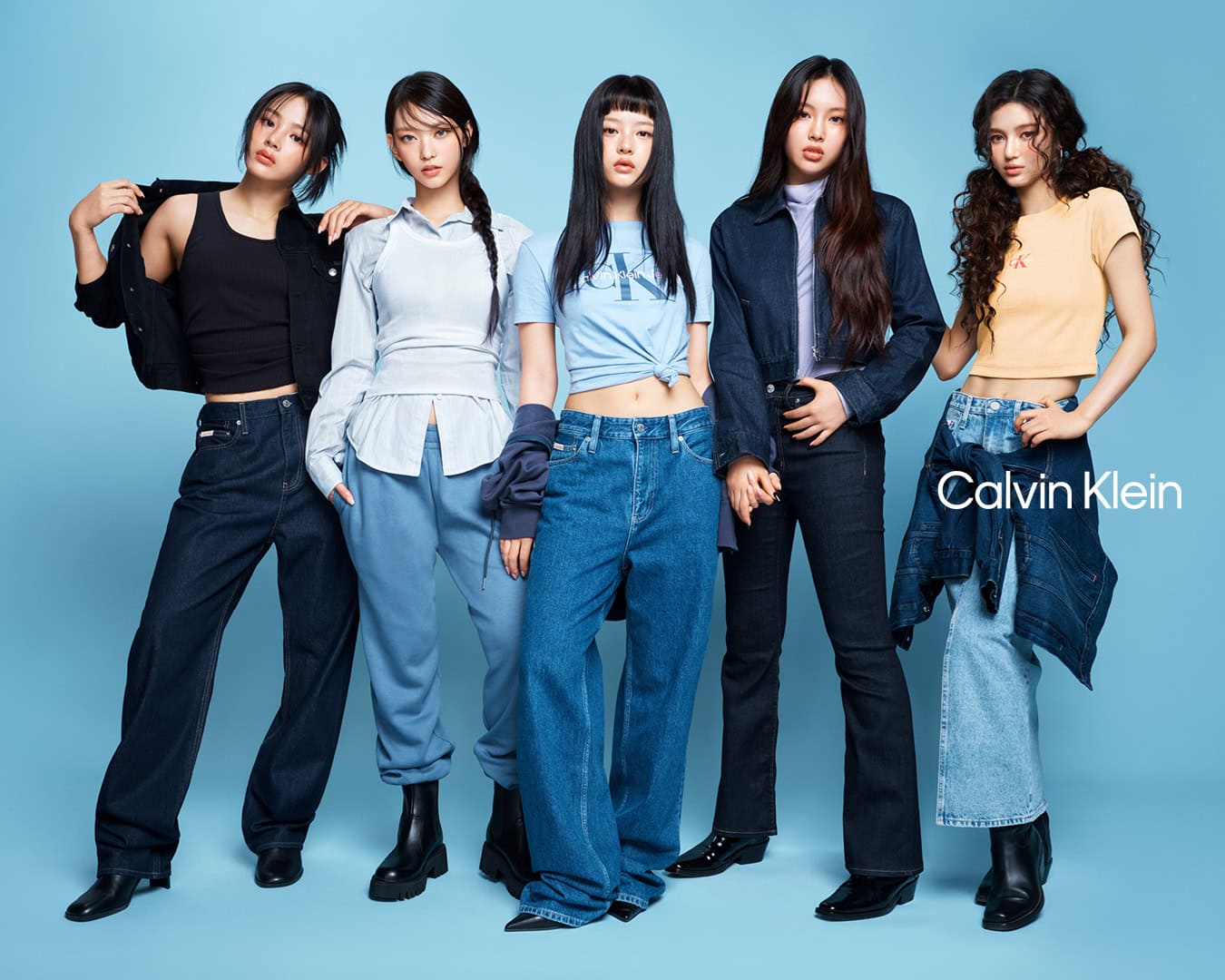 Five female models posing together against a light blue studio background for a Calvin Klein denim campaign.