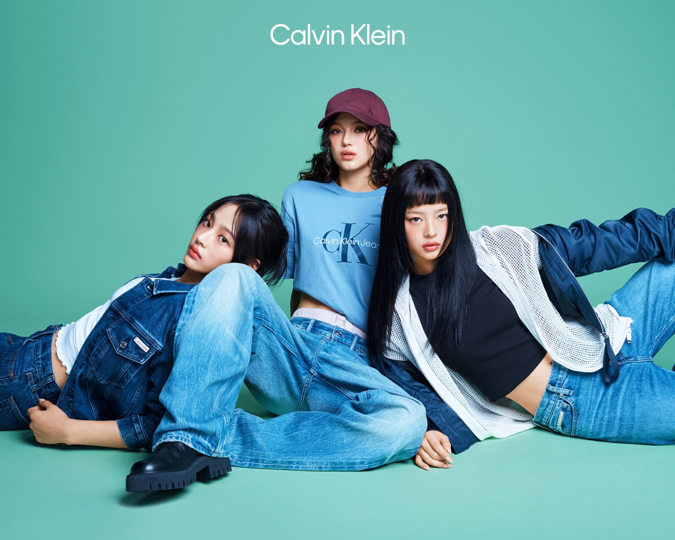 Three female models posing in casual denim streetwear and t-shirts against a solid green studio backdrop.