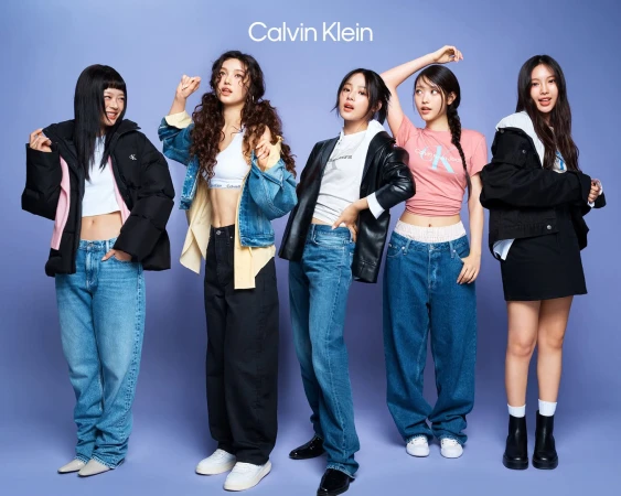 Five young female models posing against a solid purple studio background wearing Calvin Klein apparel and denim.