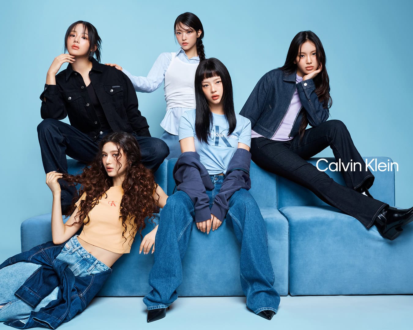 Five models posing together on a blue studio couch for a fashion campaign against a pale blue background