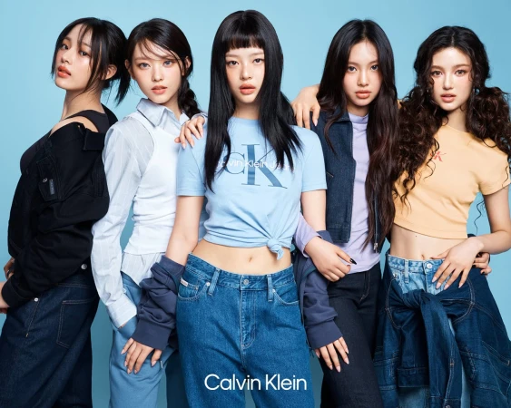 Five female models posing together against a solid blue background for a Calvin Klein denim advertising campaign.