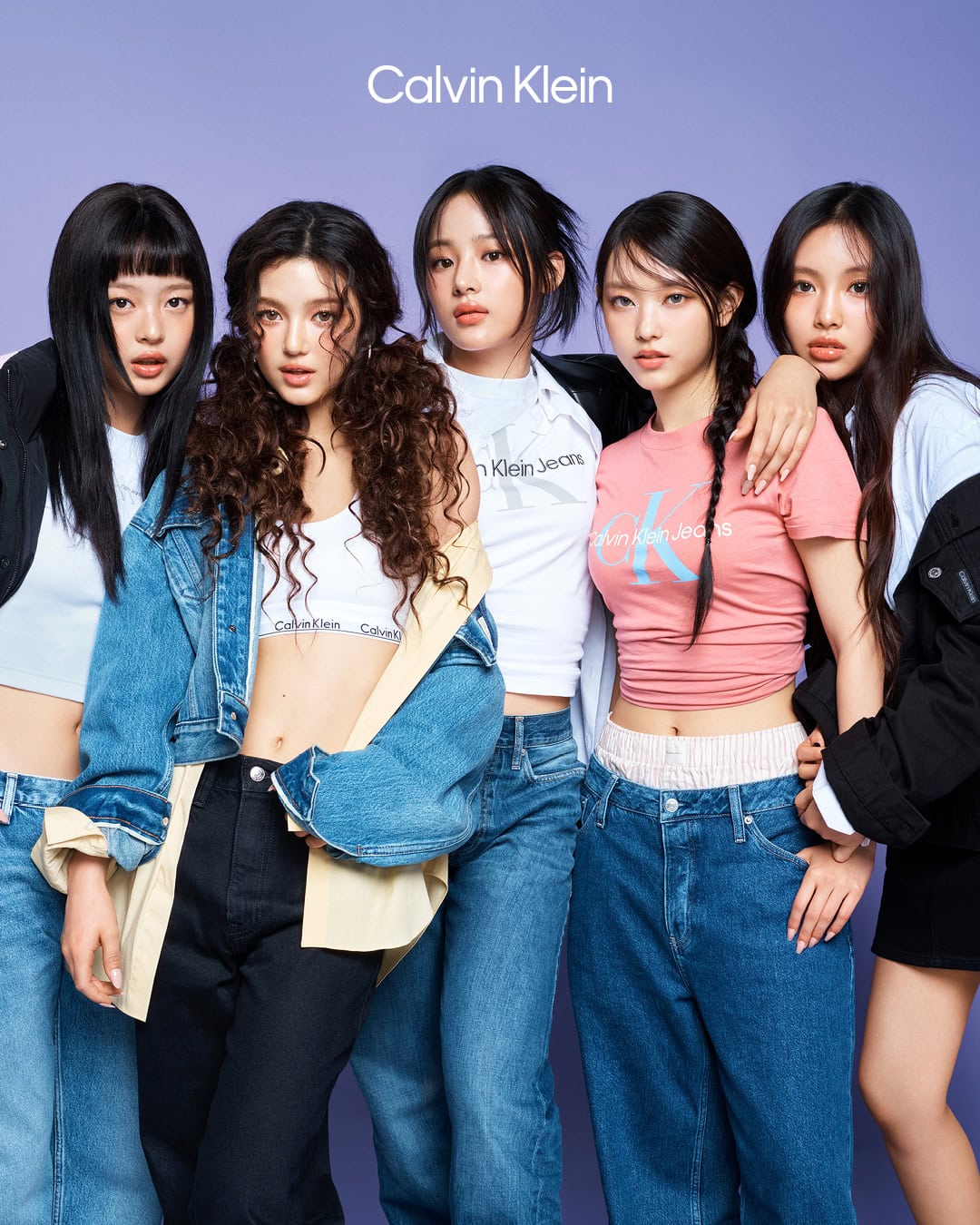 Five young female models posing together against a plain purple background for a Calvin Klein ad campaign