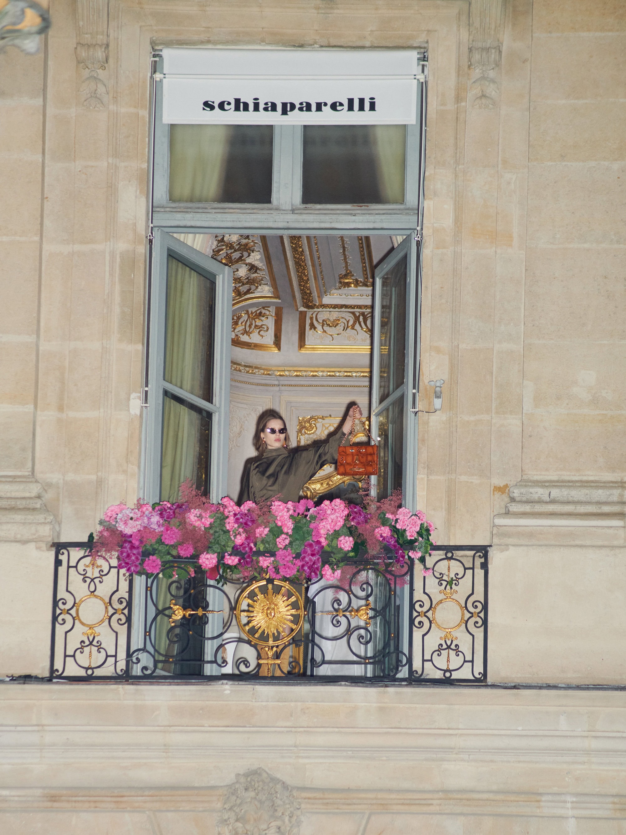 Model standing on a Parisian balcony holding a handbag in the Fall 2024 ad campaign for Schiaparelli.