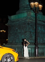 Model standing in front of Place Vendome column at night next to a lamppost and a yellow car for Schiaparelli