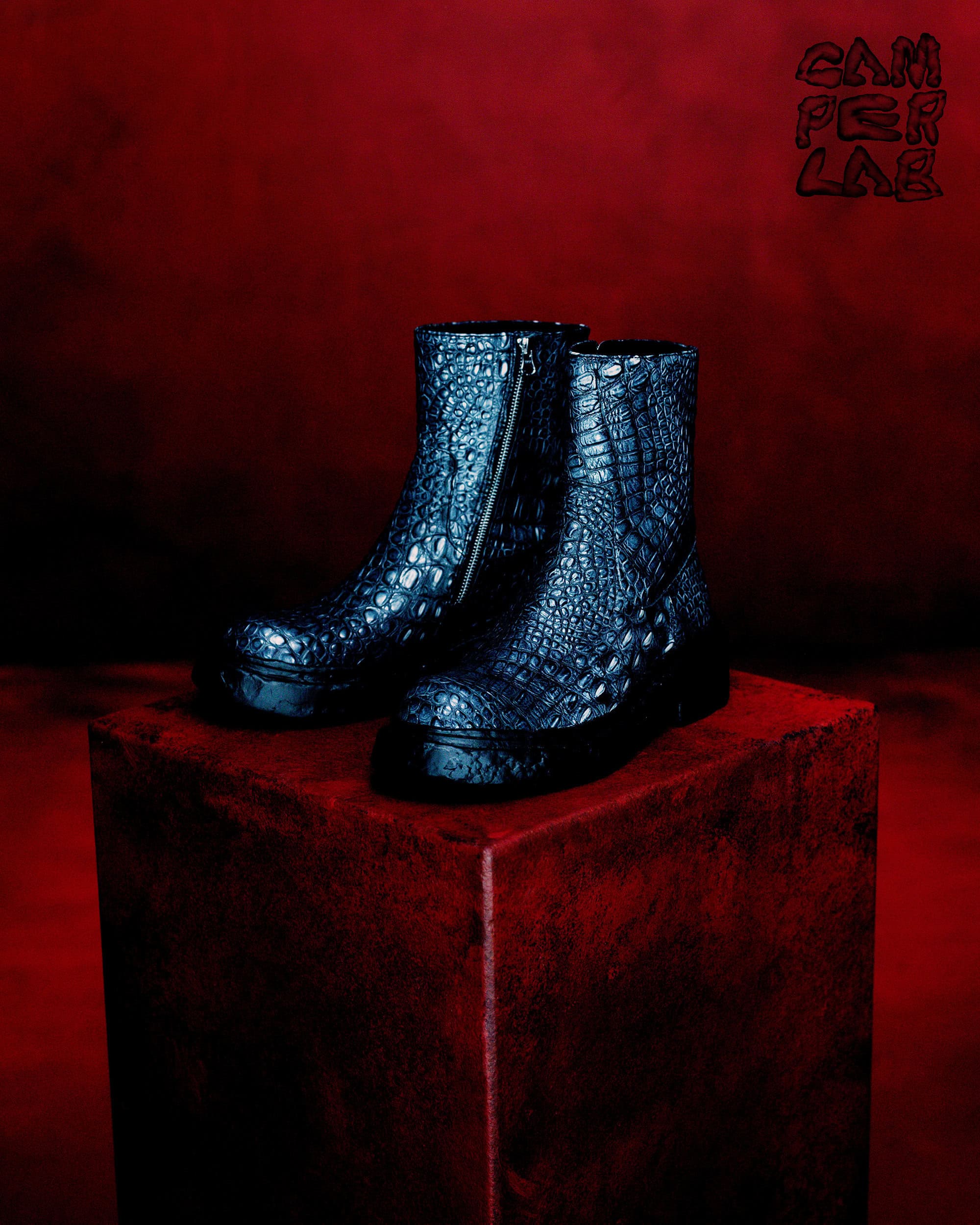 Pair of dark textured leather boots displayed on a deep red pedestal against a matching red textured background.