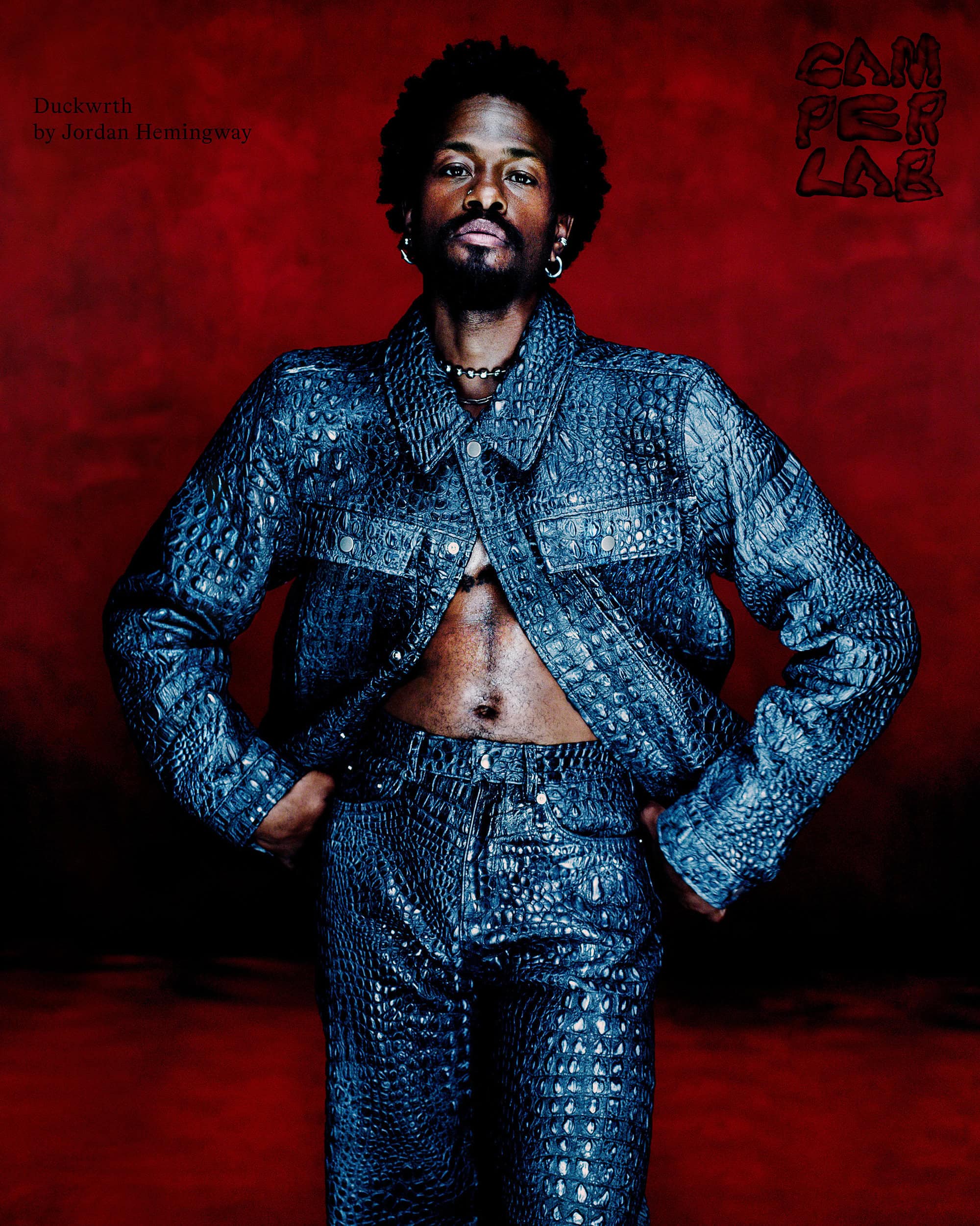 Duckwrth in textured blue denim jacket and matching pants against a moody dark red background