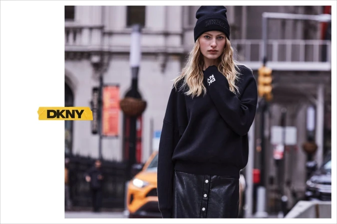 Model wearing a black beanie and sweatshirt standing on a city street with a blurred urban background