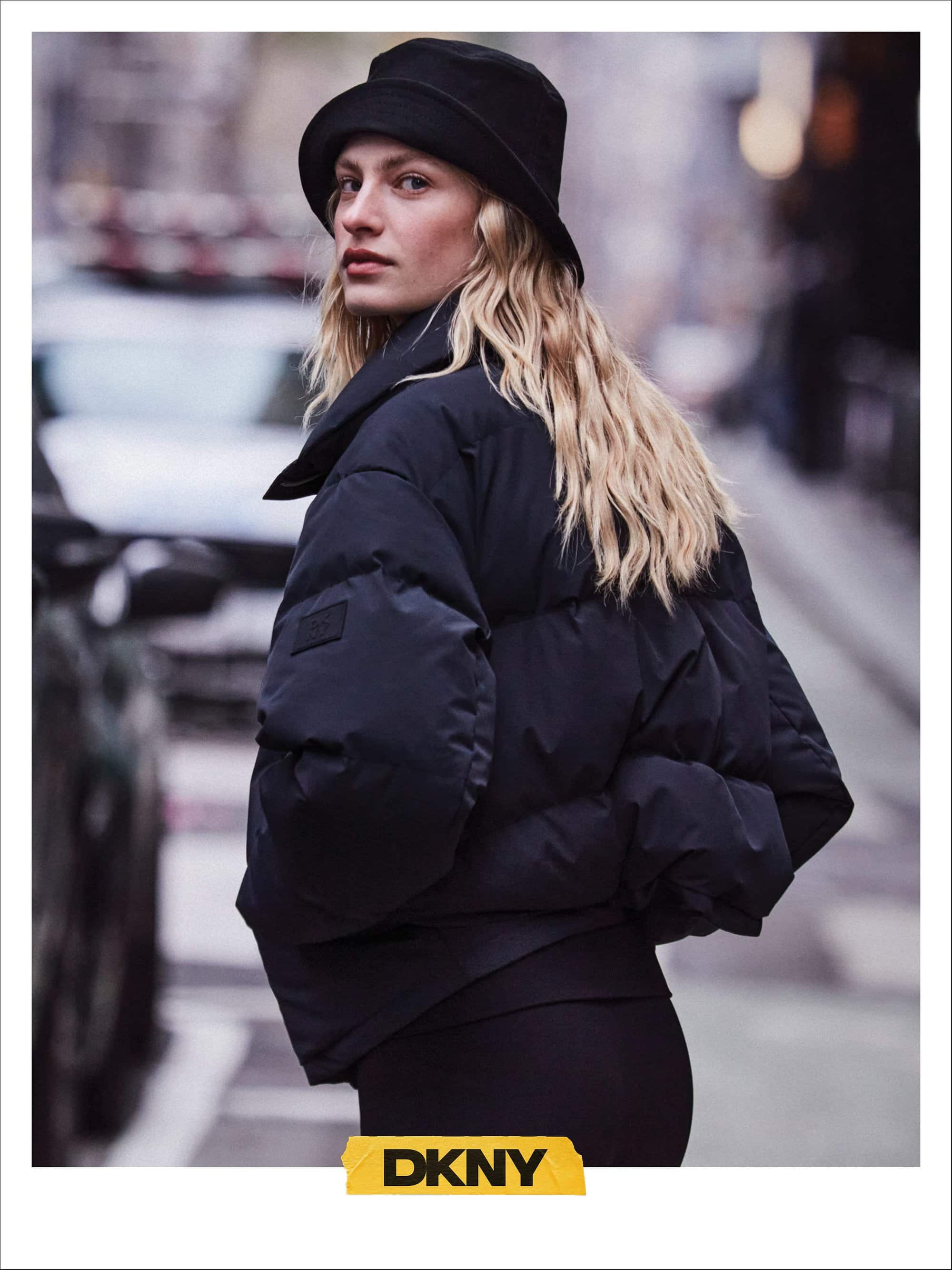 Model wearing a black puffer jacket and bucket hat on a city street for DKNY