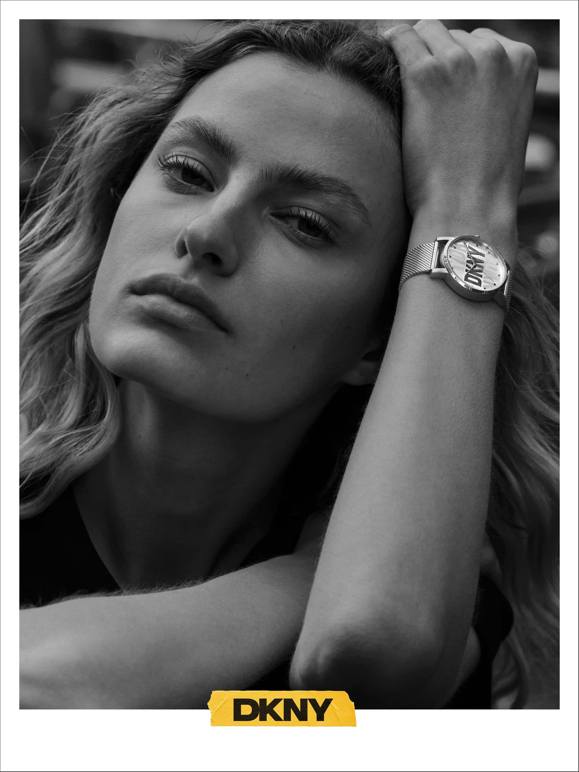 Close-up black and white portrait of a female model wearing a wristwatch with a metal mesh strap and DKNY branding.