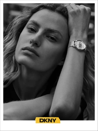 Close-up black and white portrait of a female model wearing a wristwatch with a metal mesh strap and DKNY branding.