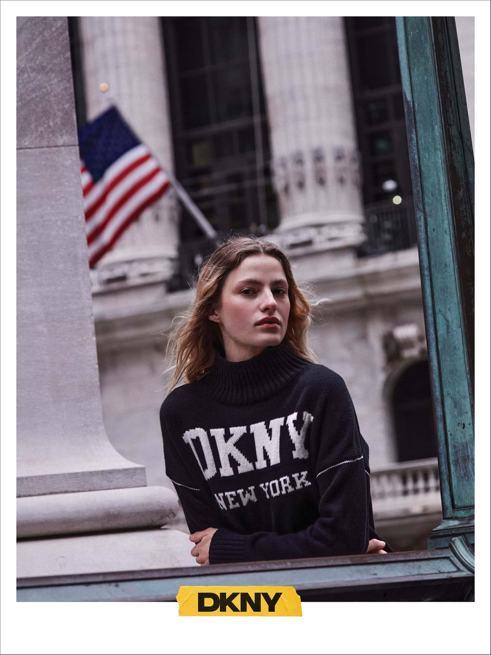 Woman wearing a black DKNY turtleneck sweater outdoors with a classical stone building and American flag in the background.