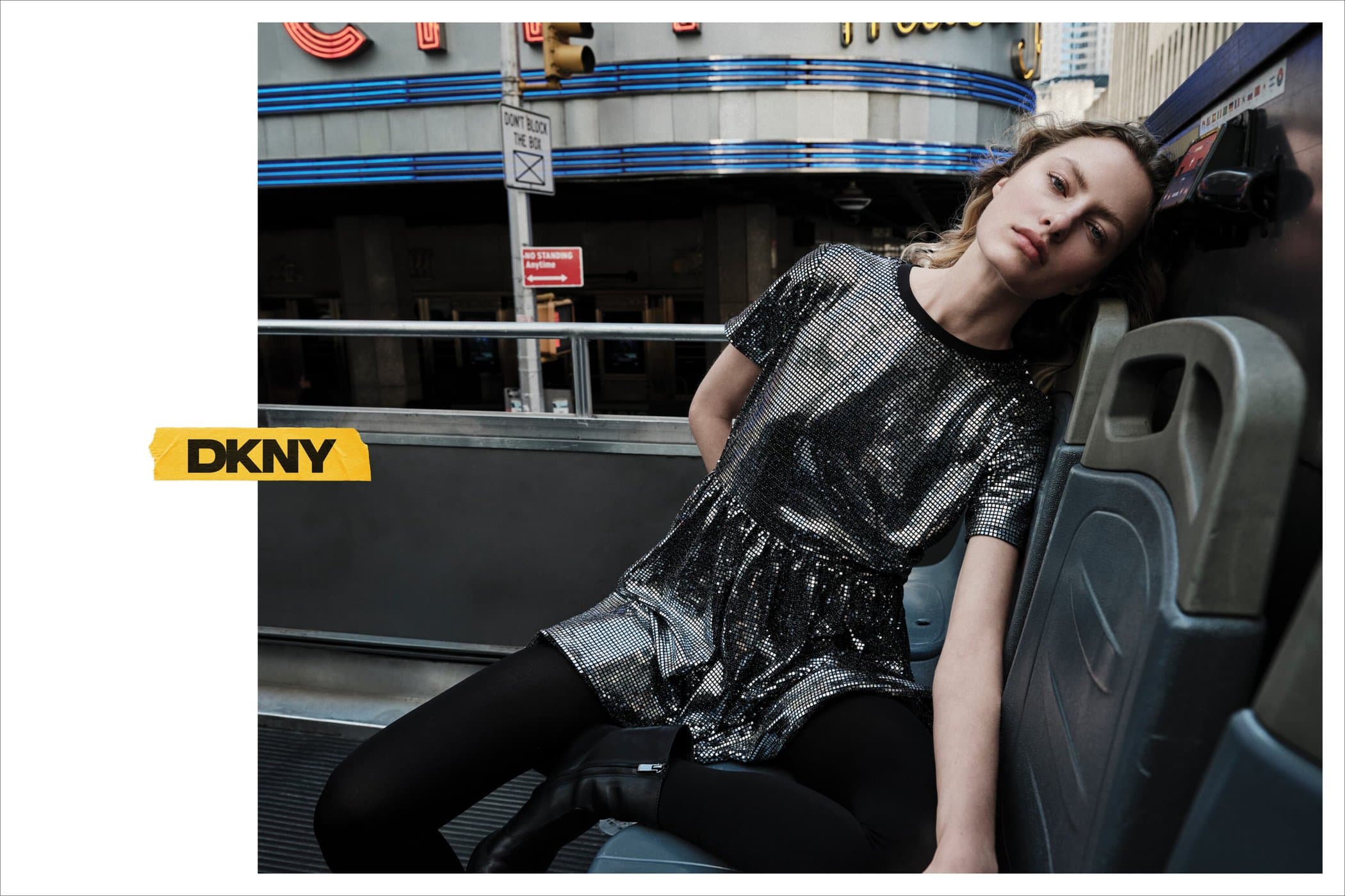 Model wearing a metallic dress and black tights seated on a bus seat in an urban setting