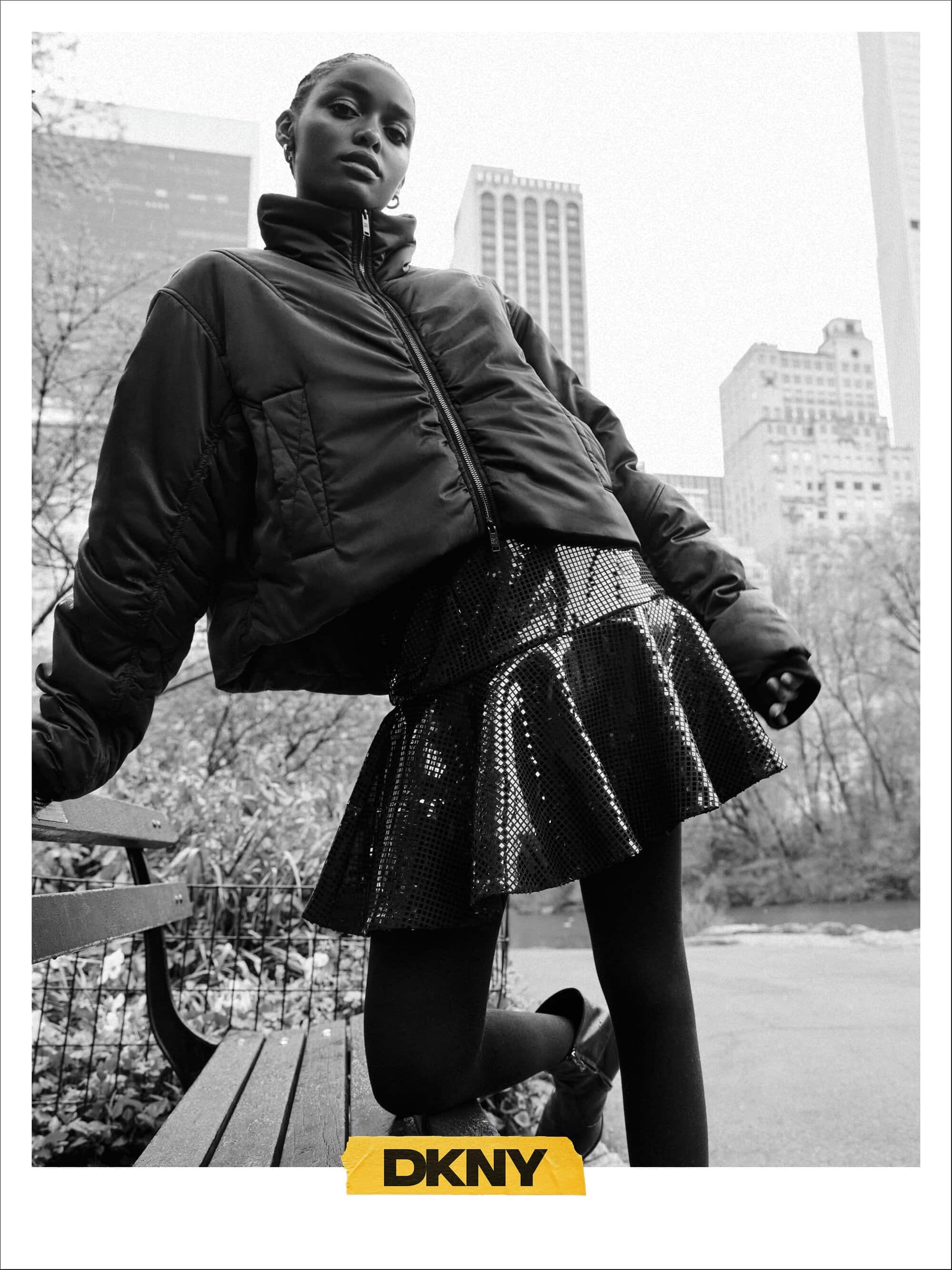 Black woman wearing a dark puffer jacket and sequin skirt outdoors in the city for the DKNY Fall 2024 ad campaign