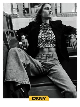 Monochrome fashion campaign image featuring a model seated in a bus wearing a sequined top and denim jeans for DKNY Fall 2024.