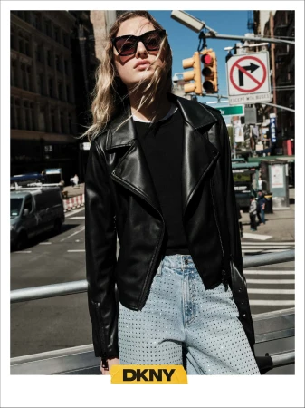 Model wearing dark sunglasses, a black leather jacket, and embellished jeans on a New York street for DKNY fall 2024 campaign.