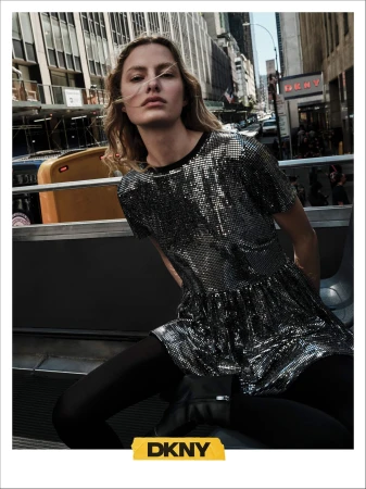 Model in shiny metallic dress and black tights seated against a New York city street background for DKNY Fall 2024 campaign