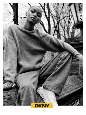 Model wearing embellished knit sweater and wide-leg denim posed near a New York subway sign for DKNY Fall 2024 campaign