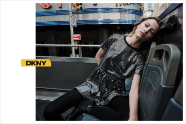 Model wearing a metallic dress and black tights seated on a bus seat in an urban setting
