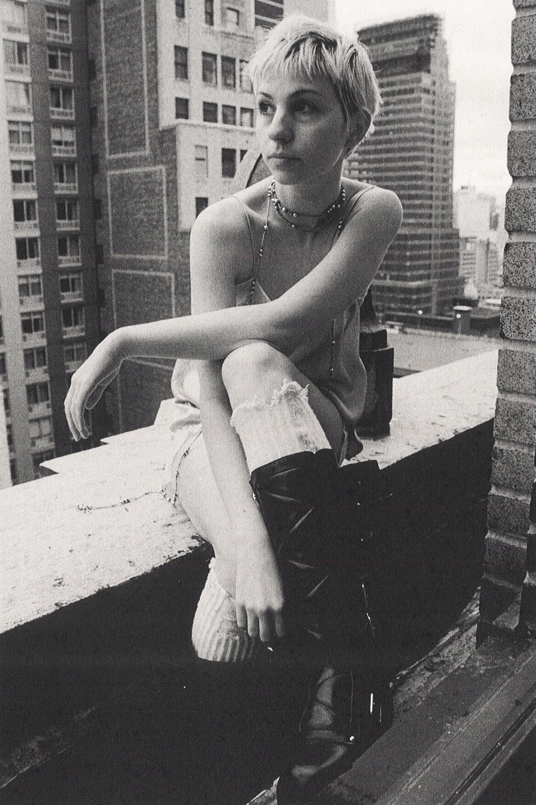 Model with short hair wearing black boots and high socks seated on a New York rooftop for Ann Demeulemeester