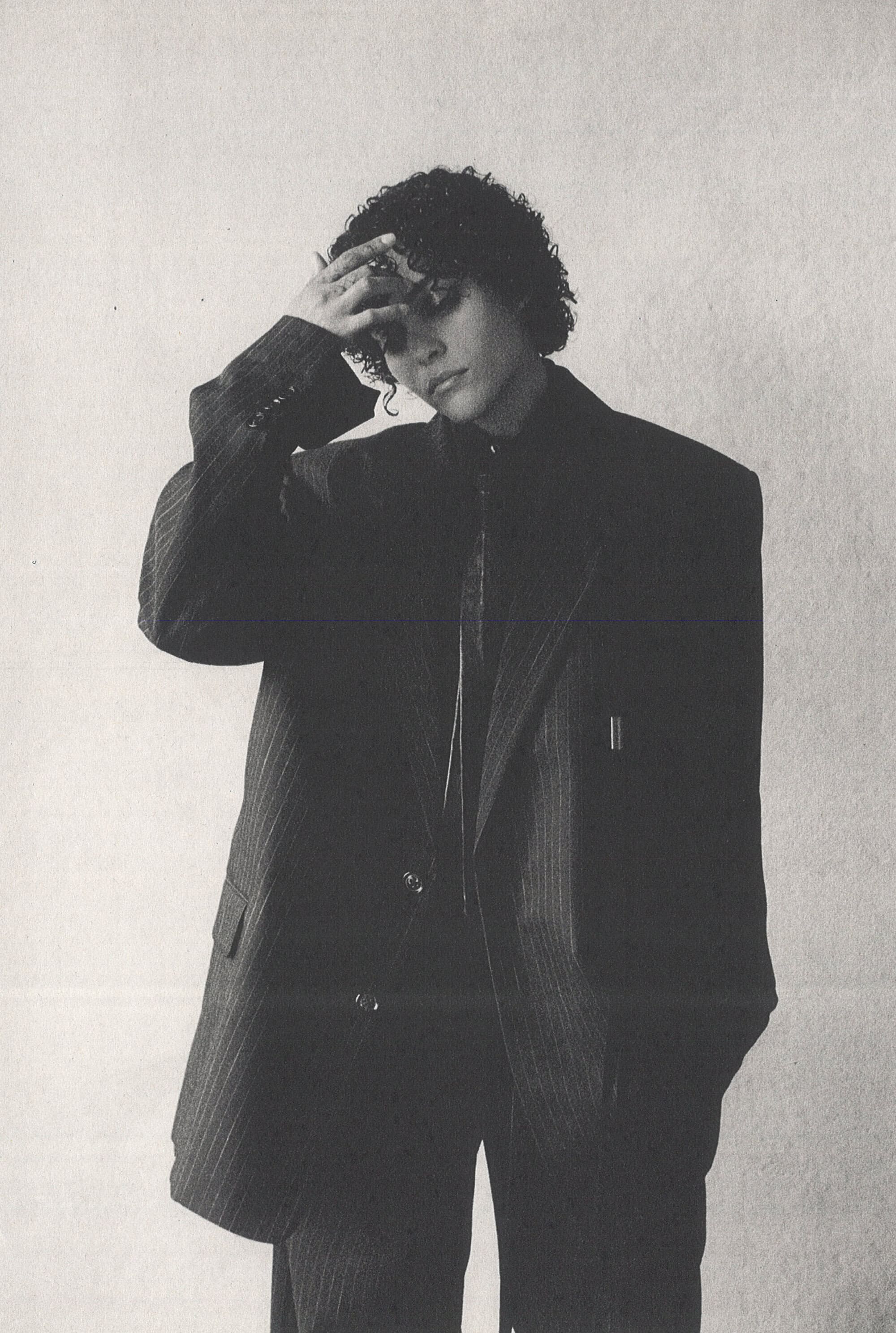 Model in oversized pinstripe suit jacket with hand on forehead against a textured light wall