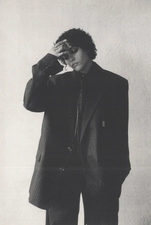 Model in oversized pinstripe suit jacket with hand on forehead against a textured light wall