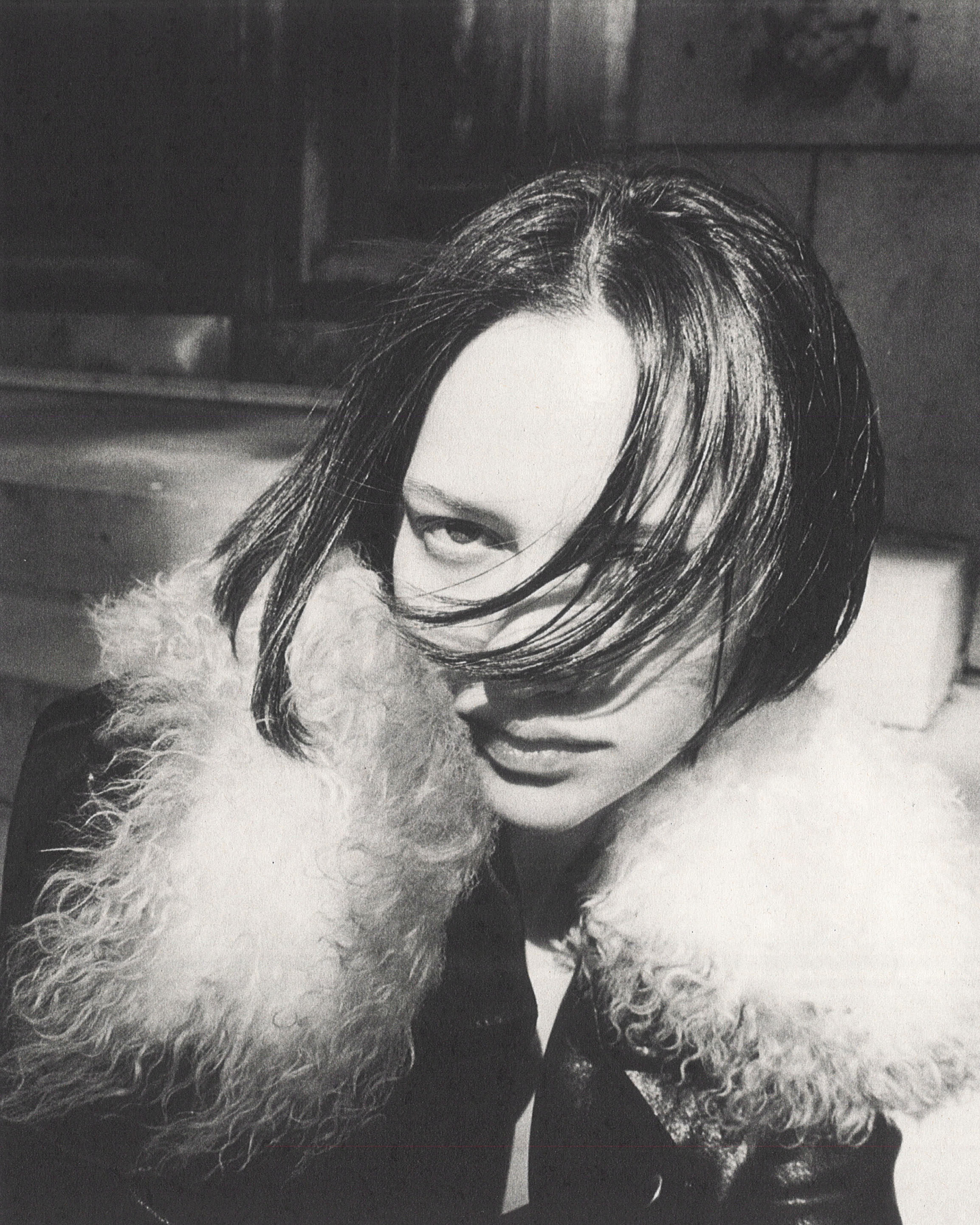 Close-up black and white portrait of a person with dark hair wearing a fluffy collar jacket outdoors in New York City.