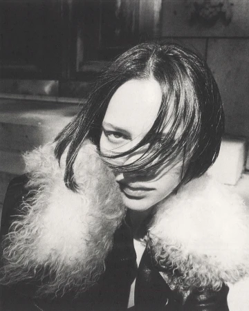 Close-up black and white portrait of a person with dark hair wearing a fluffy collar jacket outdoors in New York City.