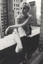 Model with short hair wearing black boots and high socks seated on a New York rooftop for Ann Demeulemeester