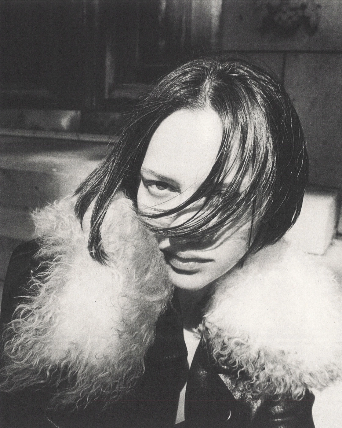 Close-up black and white portrait of a person with dark hair wearing a fluffy collar jacket outdoors in New York City.
